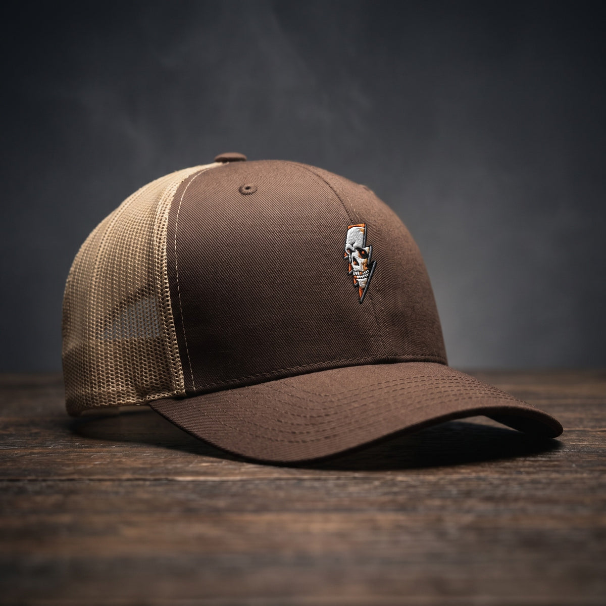 Casquette trucker Thunder Skull marron avec filet kaki et crâne éclair brodé, posée sur bois sombre