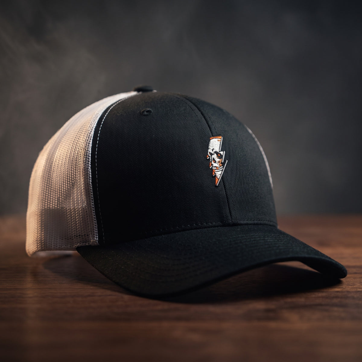 Casquette trucker Thunder Skull noire et blanche avec crâne et éclair brodés, filet blanc, posée sur bois sombre