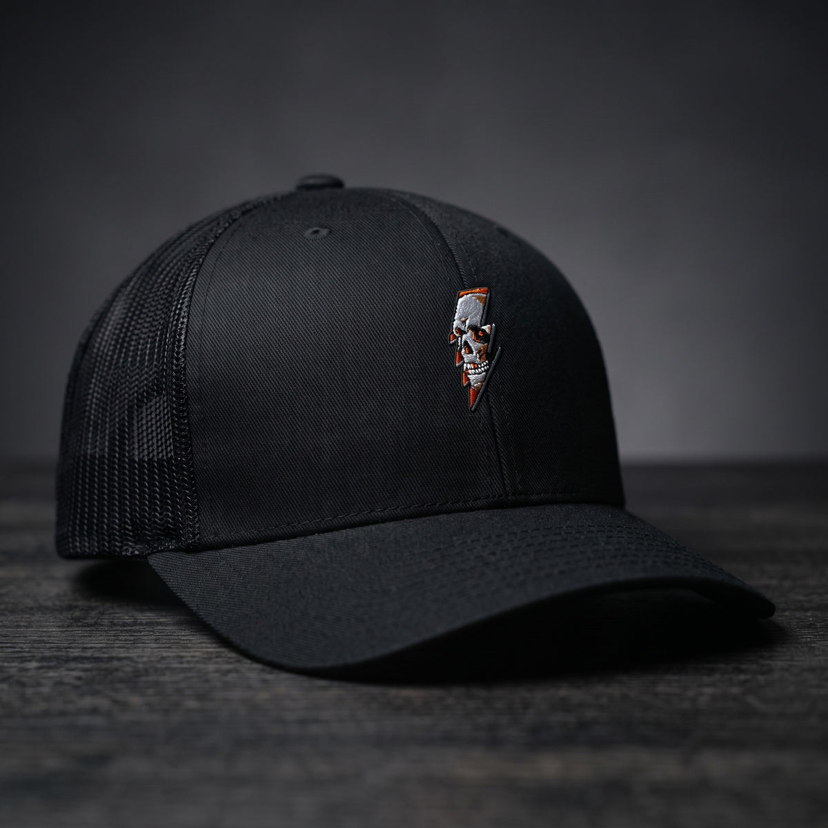 Casquette trucker Thunder Skull noire avec crâne et éclair brodés, filet noir, posée sur bois sombre