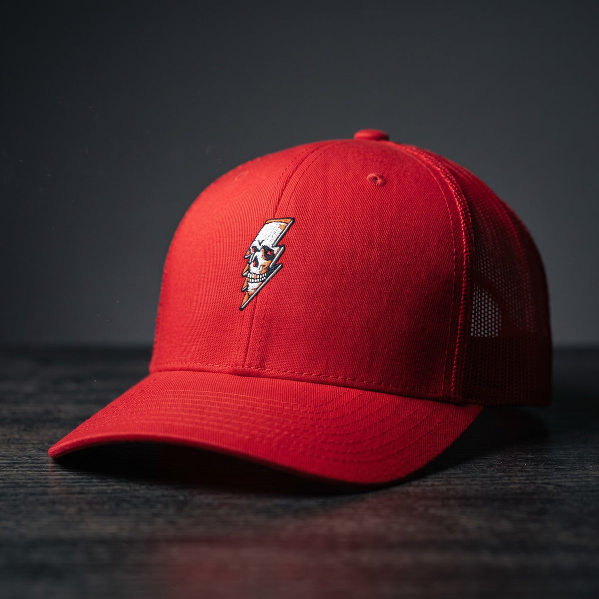 Casquette trucker Thunder Skull rouge avec crâne et éclair brodés, posée sur bois sombre
