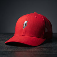 Casquette trucker Thunder Skull rouge avec crâne et éclair brodés, posée sur bois sombre