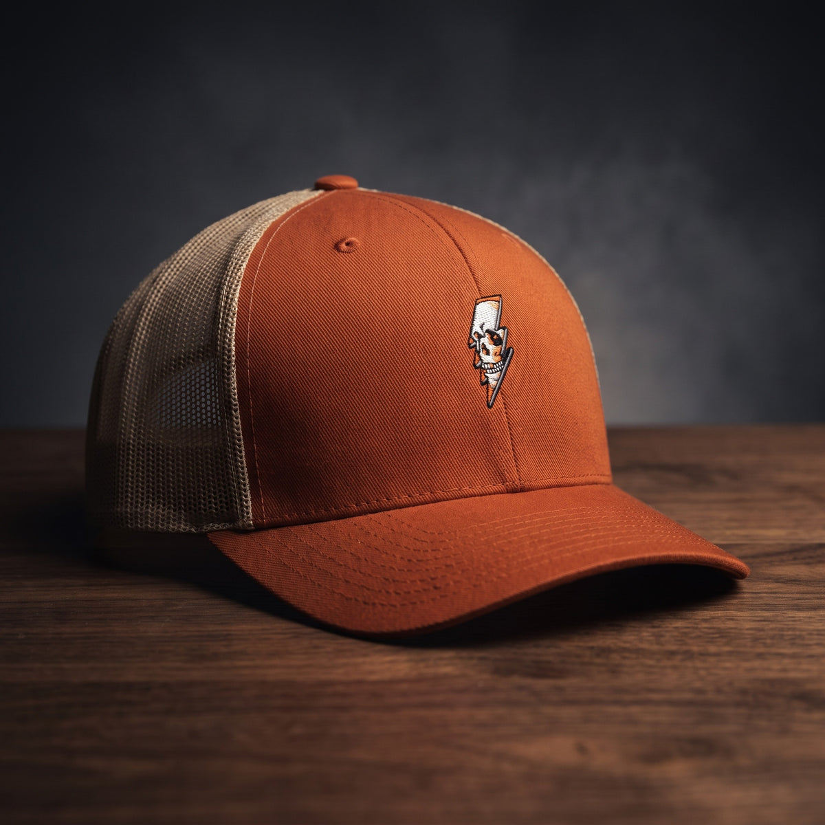 Casquette trucker Thunder Skull roux orangé avec filet kaki et crâne éclair brodé, posée sur bois sombre