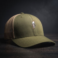 Casquette trucker Thunder Skull vert mousse avec filet kaki et crâne éclair brodé, posée sur bois sombre