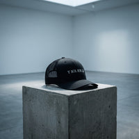 Casquette trucker noire « Y N'A RIN LÀ » posée seule sur un socle en béton dans une galerie d'art complètement vide