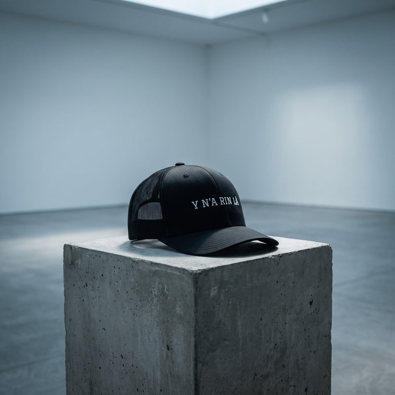 Casquette trucker noire « Y N'A RIN LÀ » posée seule sur un socle en béton dans une galerie d'art complètement vide