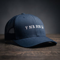 Casquette trucker bleu marine brodée « Y N'A RIN LÀ » en blanc, posée sur un bois sombre
