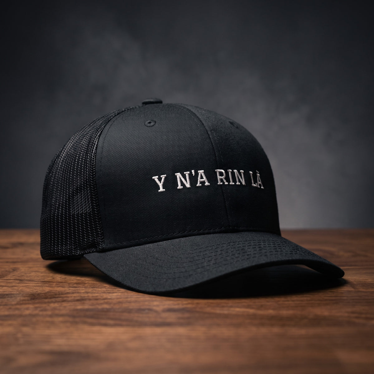 Casquette trucker noire brodée « Y N'A RIN LÀ » en blanc, posée sur un bois sombre