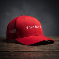 Casquette trucker rouge brodée « Y N'A RIN LÀ » en blanc, posée sur un bois sombre