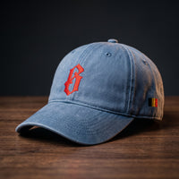 Casquette belge originale brodée B gothique rouge, coloris bleu jean, posée sur bois foncé, vue trois-quarts