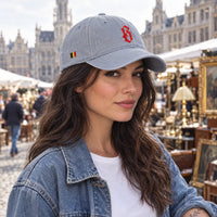 Casquette belge gris granit brodée B rouge portée par une femme sur un marché aux puces bruxellois