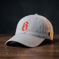 Casquette belge originale brodée B gothique rouge, coloris gris granit, posée sur bois foncé, vue trois-quarts
