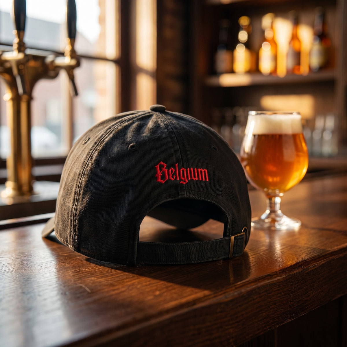Casquette belge noire brodée Belgium rouge au dos, posée sur le comptoir d'un café belge à côté d'une bière