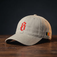 Casquette belge originale brodée B gothique rouge, coloris sable, posée sur bois foncé, vue trois-quarts