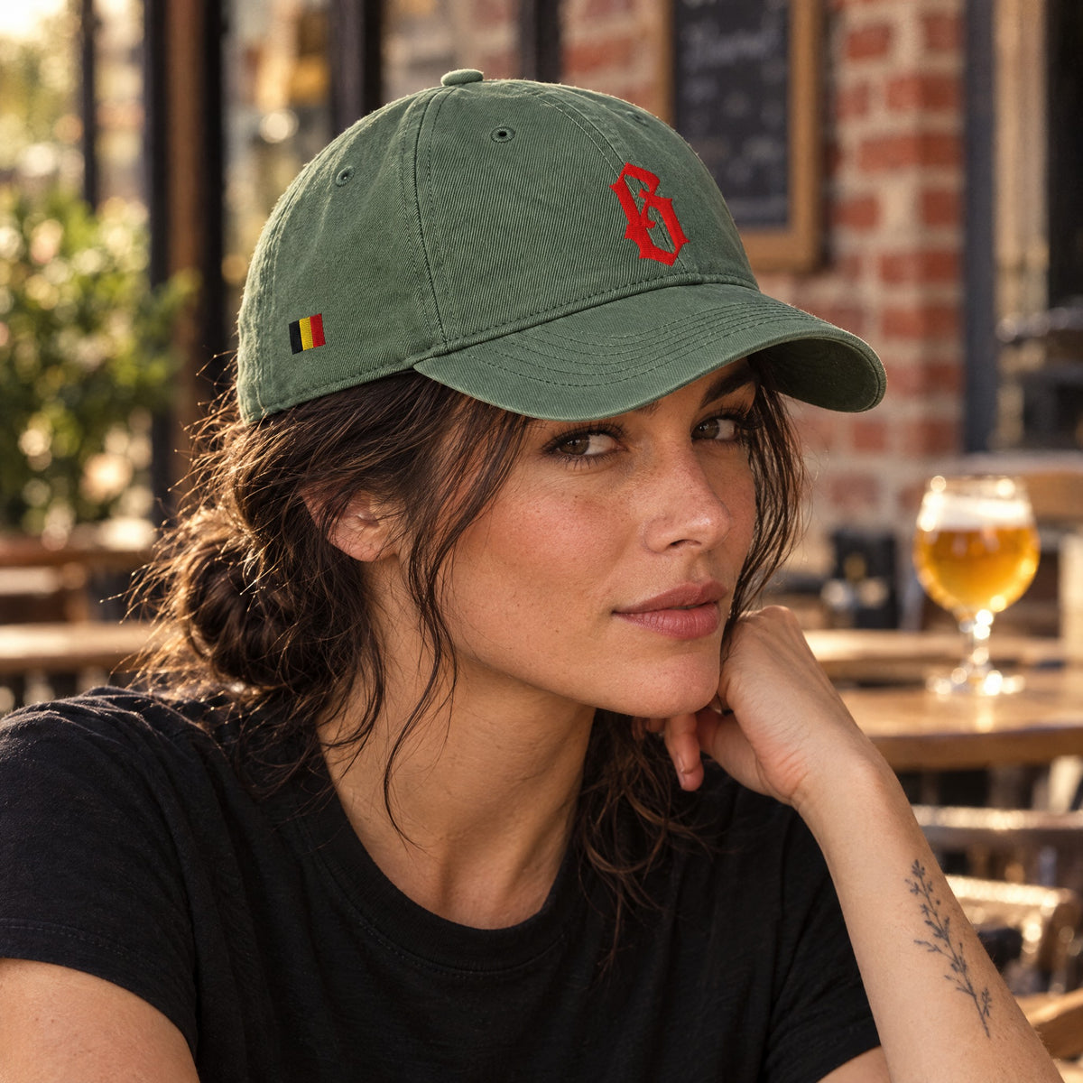 Casquette belge vert mousse brodée B rouge portée par une femme en terrasse de café belge