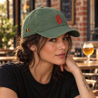 Casquette belge vert mousse brodée B rouge portée par une femme en terrasse de café belge