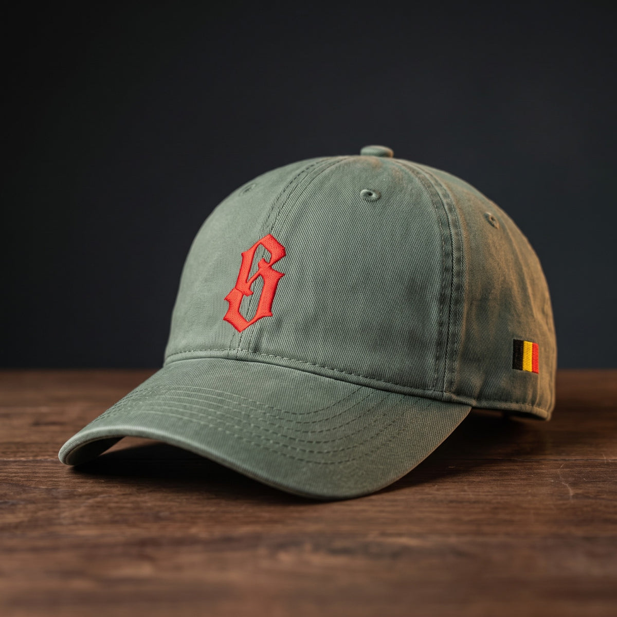 Casquette belge originale brodée B gothique rouge, coloris vert mousse, posée sur bois foncé, vue trois-quarts
