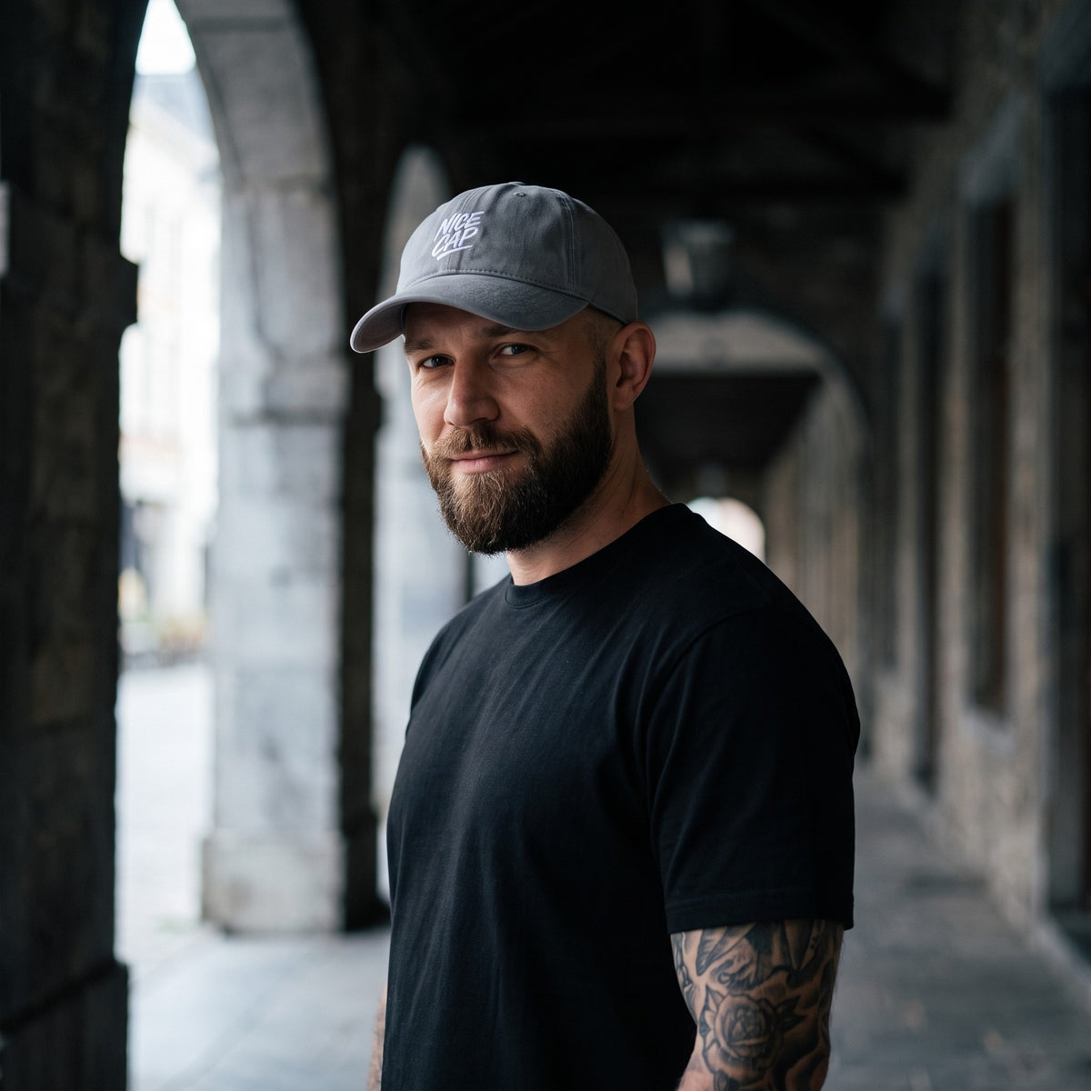 Casquette délavée dad cap vintage gris granit portée par un homme sous un passage en pierre