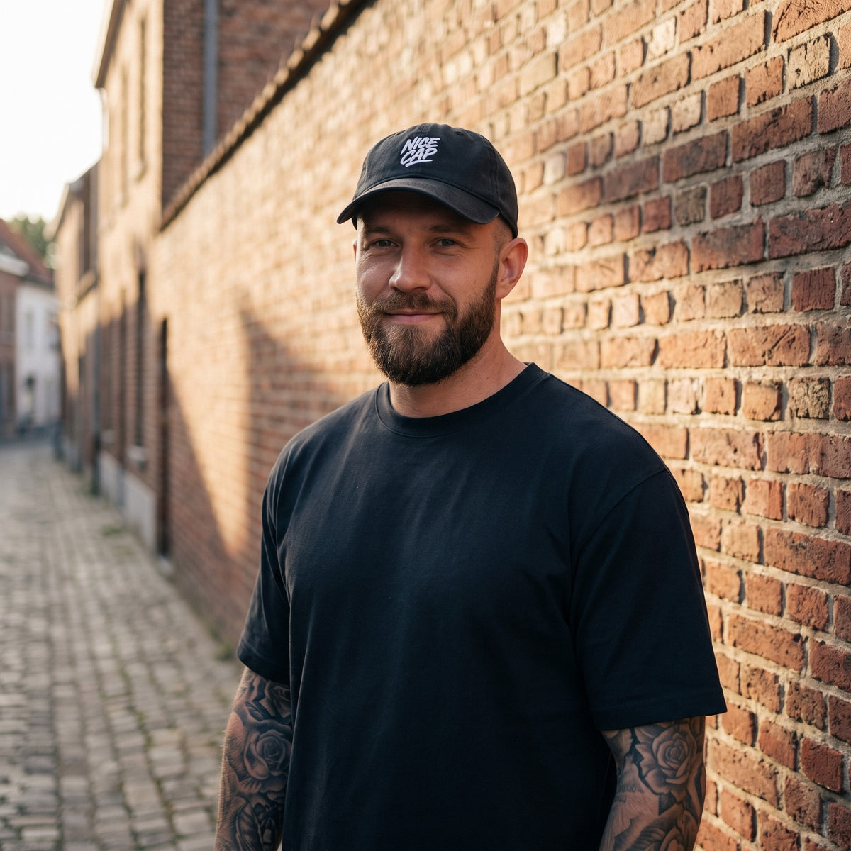 Casquette délavée dad cap vintage noire portée par un homme devant un mur de briques belge