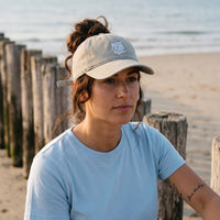 Casquette délavée dad cap vintage sable portée par une femme devant un brise-lames en bois