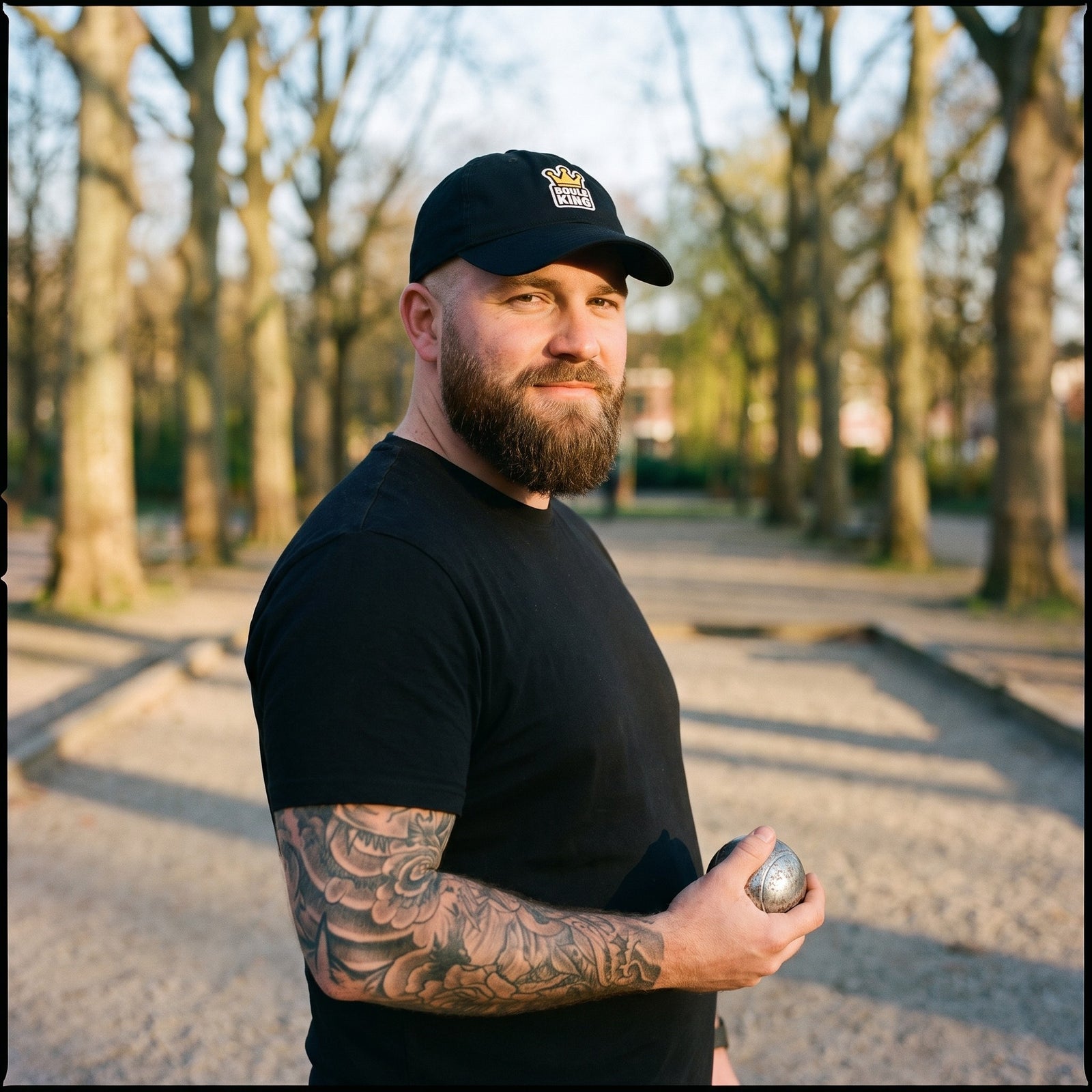 Homme portant la casquette de pétanque originale Boule King noire sur un terrain de pétanque