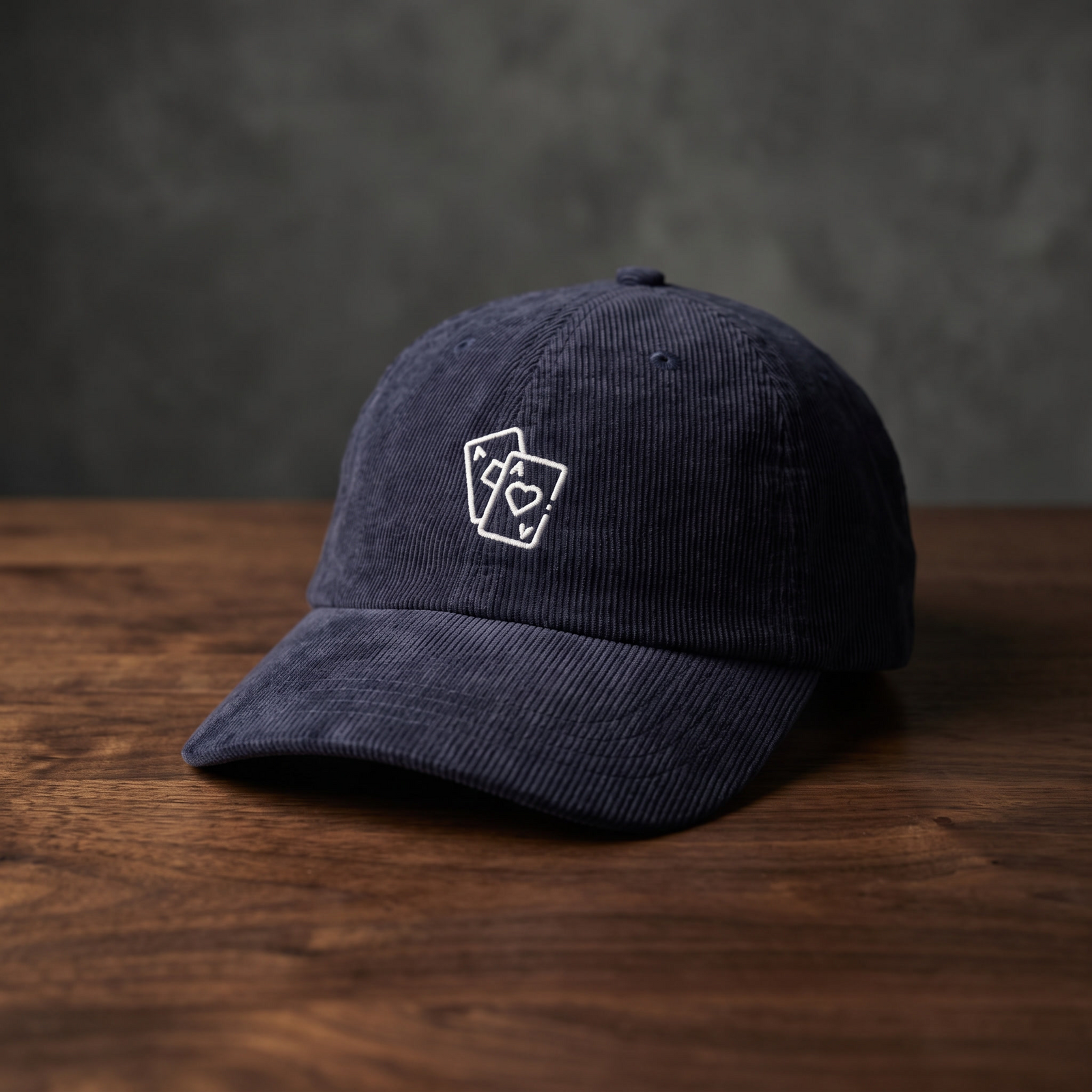 Casquette poker « Paire d'As » bleu marine en velours côtelé, as de pique et as de cœur brodés, posée sur bois foncé