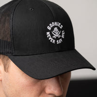 Gros plan de la broderie Goonies Never Say Die sur la casquette trucker noire portée