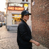 Casquette Goonies Never Say Die noire portée par une femme devant une friterie belge