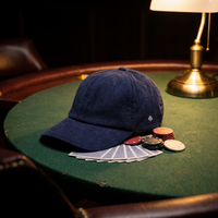 Casquette en velours côtelé navy brodée As de Pic, posée sur une table de poker avec cartes et jetons