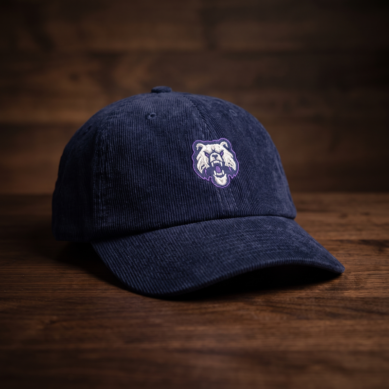 Casquette en velours côtelé bleu marine CHT'M brodée d'une tête de bulldog grondant blanche et grise à contour violet, présentée sur fond bois noyer foncé