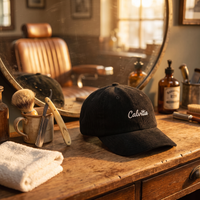 Casquette en velours côtelé noire « Calvitie » posée sur un comptoir de barbier vintage, entre rasoir et blaireau, ambiance dorée rétro CHT'M Boutique.
