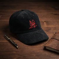 Casquette en velours côtelé noire brodée Cap, CHT'M Boutique, mise en scène stylo plume et carnet en cuir sur bois de noyer foncé