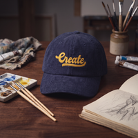Casquette en velours côtelé bleu marine 'Create' mise en scène dans un atelier d'artiste avec pinceaux et palette de peinture
