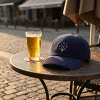 Casquette belge en velours côtelé DAD posée sur une table de terrasse de café belge, à côté d'une bière, lumière dorée de fin de journée, CHT'M Boutique.
