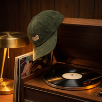 Casquette velours côtelé Daddy Cool posée sur un tourne-disque vintage, ambiance rétro 70s, CHT'M Boutique.