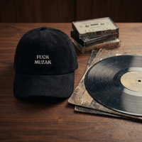 Casquette dad cap en velours côtelé noir FUCK MUZAK posée sur bois avec vinyle et cassettes vintage