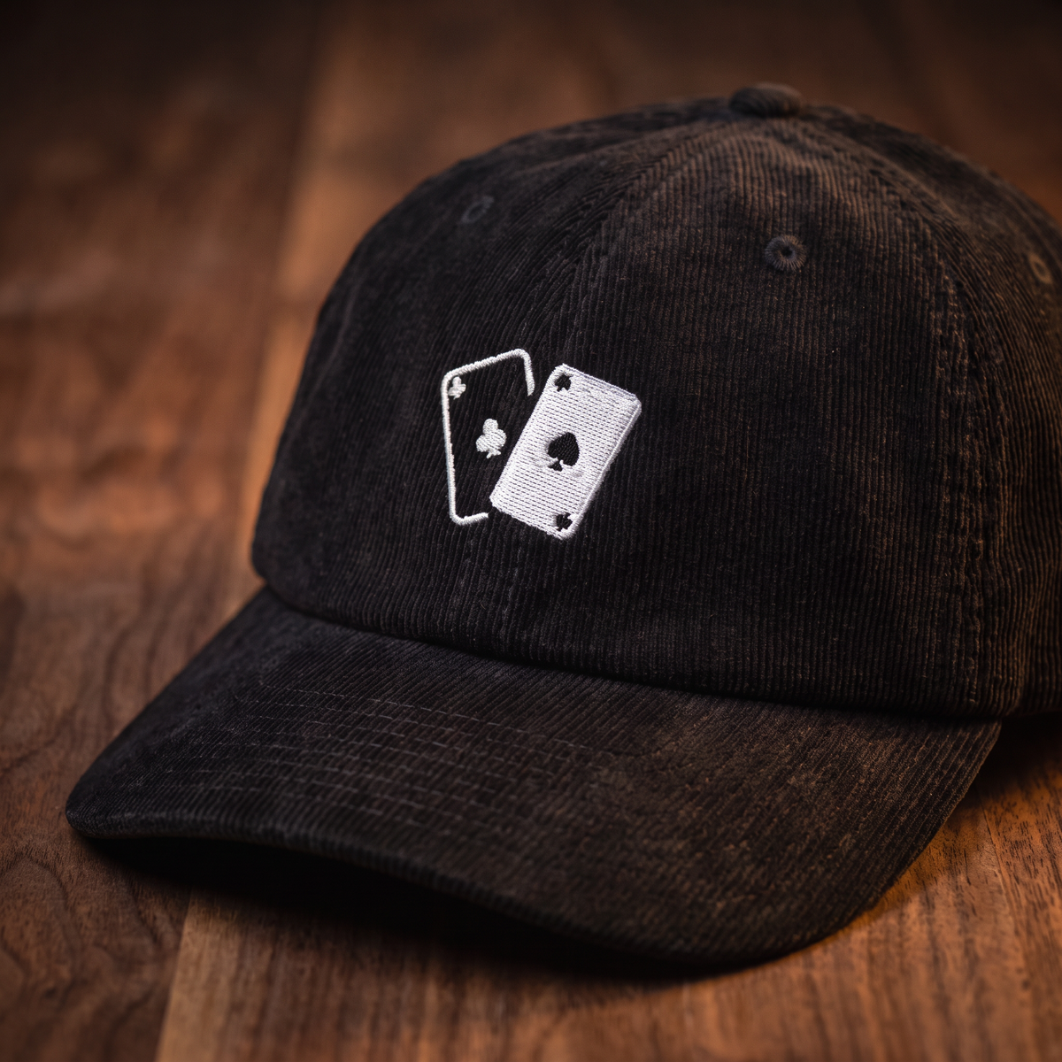Casquette en velours côtelé motif jeu de cartes, coloris noir, vue trois-quarts rapprochée sur fond bois noyer foncé