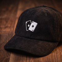 Casquette en velours côtelé motif jeu de cartes, coloris noir, vue trois-quarts rapprochée sur fond bois noyer foncé