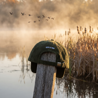 Casquette velours côtelé Les Oies Sauvages, vue de dos avec broderie « Vers le Midi », posée dans un marais brumeux à l'aube avec des oies sauvages en vol, CHT'M Boutique.