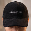 Gros plan de la broderie blanche « Pas évident hein » sur la casquette velours côtelé noire portée
