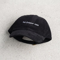 Casquette dad hat velours côtelé noire « Pas évident hein » posée à plat, design complet