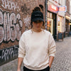 Femme en ruelle belge portant la casquette originale « Pas évident hein » en velours côtelé noir
