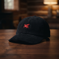 Casquette en velours côtelé noire CHT'M brodée d'un pégase rouge (cheval ailé au galop), présentée sur fond bois noyer foncé