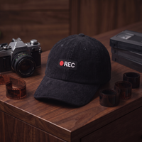 Casquette en velours côtelé noire CHT'M avec broderie 'REC', mise en scène avec caméra vintage et bobines de film