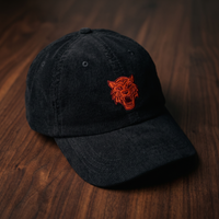 Casquette en velours côtelé noire brodée tête de tigre, CHT'M Boutique, vue légèrement de trois-quarts sur bois de noyer foncé