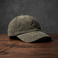 Casquette en velours côtelé olive avec trèfle brodé, vue de profil sur bois foncé