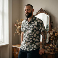 Chemise homme manches courtes noire à pivoines blanches portée par un homme près d'un miroir ancien et d'une coiffeuse vintage - CHT'M Boutique