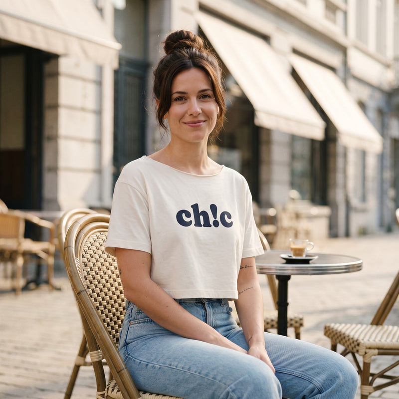 Crop top femme épaules dénudées blanc à ourlet roulé, print ch!c, porté en terrasse de café belge