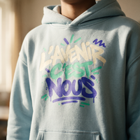 Gros plan du graffiti L'avenir c'est nous sur le hoodie oversize bleu ciel porté