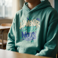 Gros plan du graffiti L'avenir c'est nous sur le hoodie oversize vert jade porté