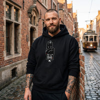 Homme tatoué portant le hoodie oversize original noir Hope dans une rue pavée belge, tram en arrière-plan